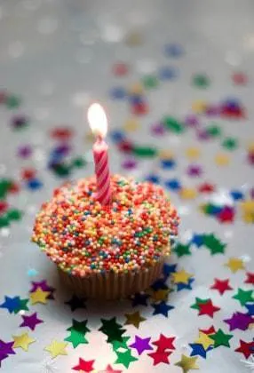 Birthday cupcake on silver paper, with one candle, and sprinkles.